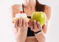 Close up portrait of a sportswoman holding cupcake and an apple isolated over white background