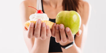 Close up portrait of a sportswoman holding cupcake and an apple isolated over white background